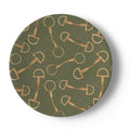 A round decorative plate featuring a repeating pattern of gold horse bits and rings over an olive green background with a subtle dotted diamond grid.