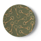 A round decorative plate featuring a repeating pattern of gold horse bits and rings over an olive green background with a subtle dotted diamond grid.