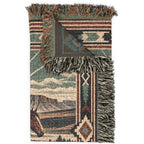 A folded woven throw blanket with a Southwestern geometric pattern and fringe, featuring a horse motif and mountain landscape design, shown on a white background.
