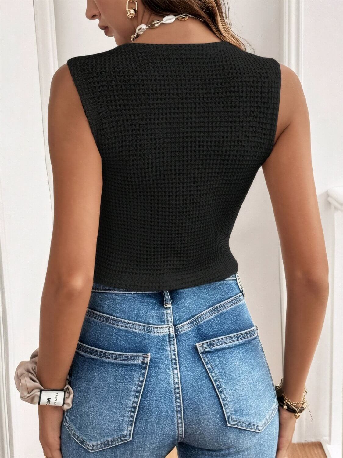 Person wearing a black sleeveless vest and blue jeans indoors.