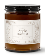 A 9 oz soy wax candle in a amber glass jar, a cream label with botanical illustrations, and a black metal lid. The label reads 'REAL COOL COMPANY' and 'Apple Harvest'.