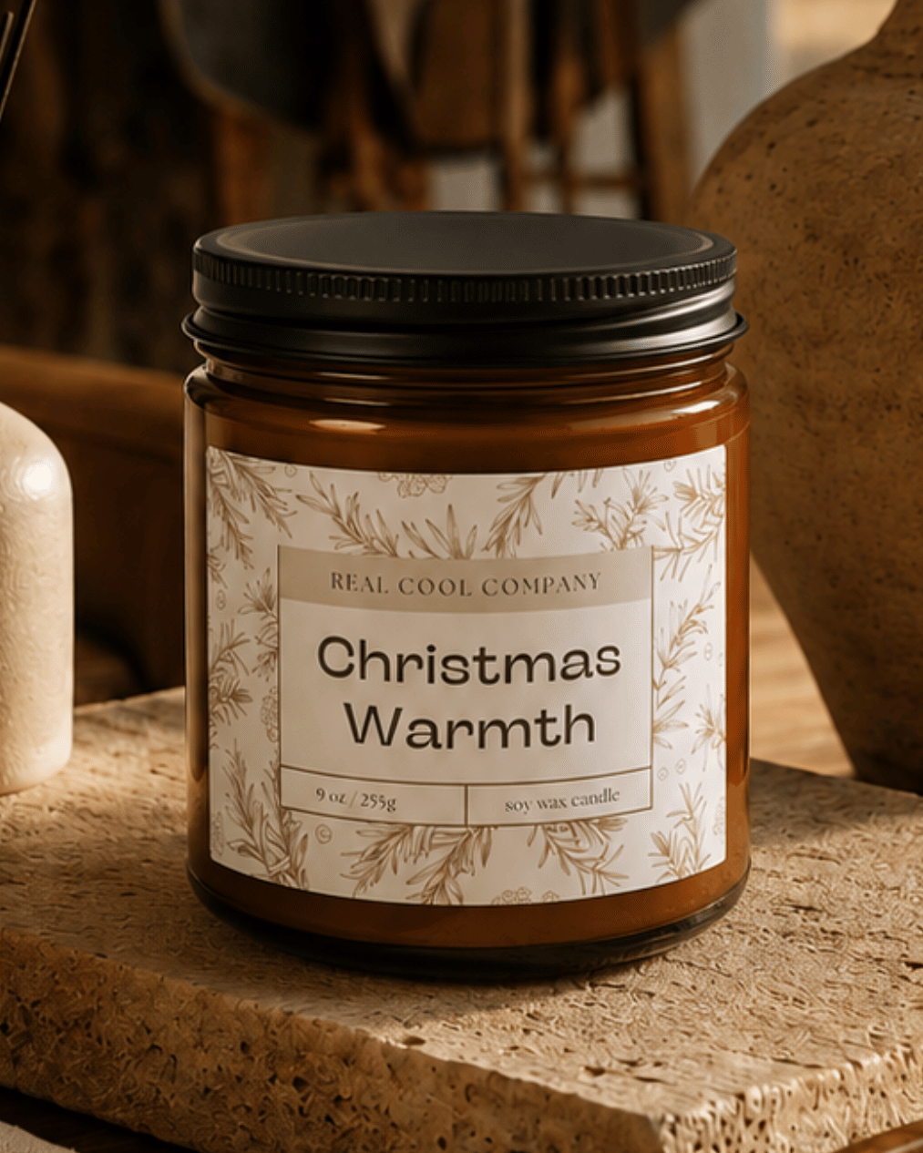 A jar candle labeled 'Christmas Warmth' by Red Cedar Company sits on a stone slab in a rustic, warm-toned interior setting with dried grasses, a ceramic vase, and wooden decor.