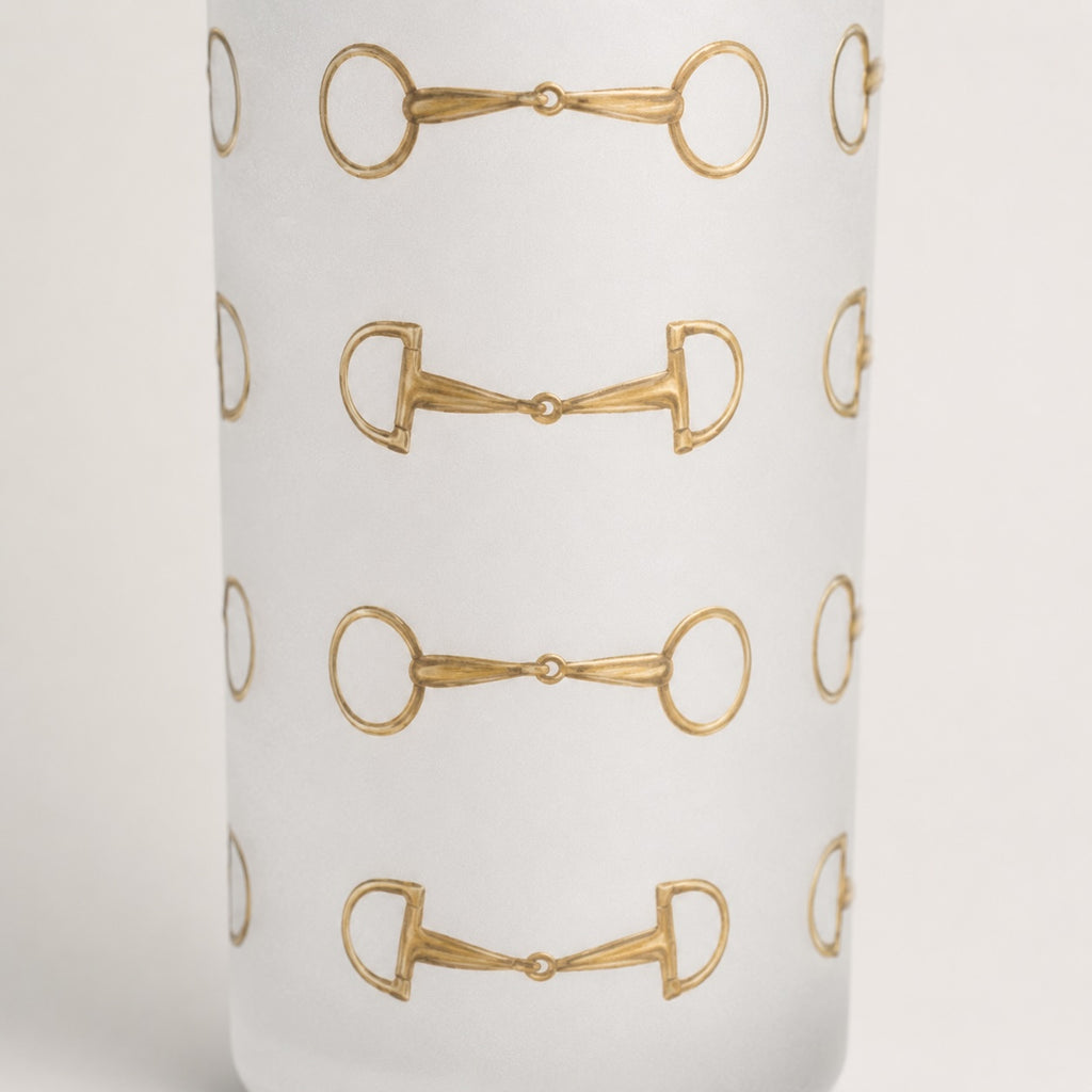 A closeup of a frosted shot glass  featuring a repeating horsebit pattern, shown against a clean white background.