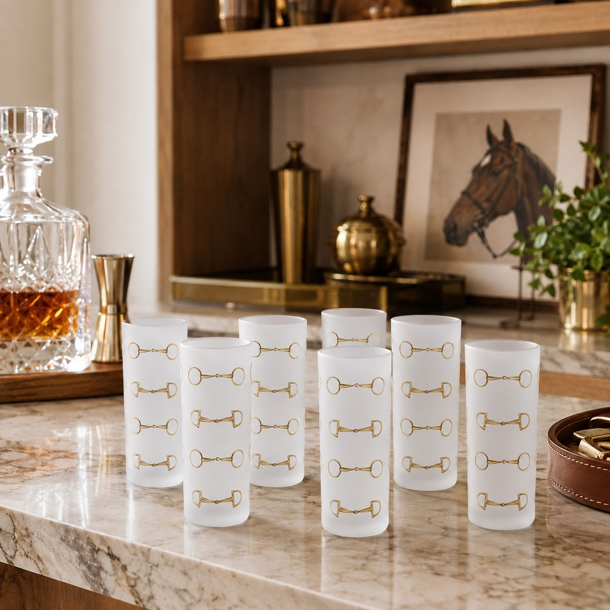 Six frosted glass shot glasses with gold horse-bit patterns arranged on a marble bar counter in a warm, stylish bar setting.