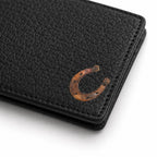 A close-up of a black pebbled leather wallet featuring a metallic bronze horseshoe emblem on the front, set against a clean white background.