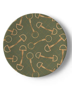 A round decorative plate featuring an all-over pattern of gold horse bits on an olive green background with a subtle dotted diamond grid.