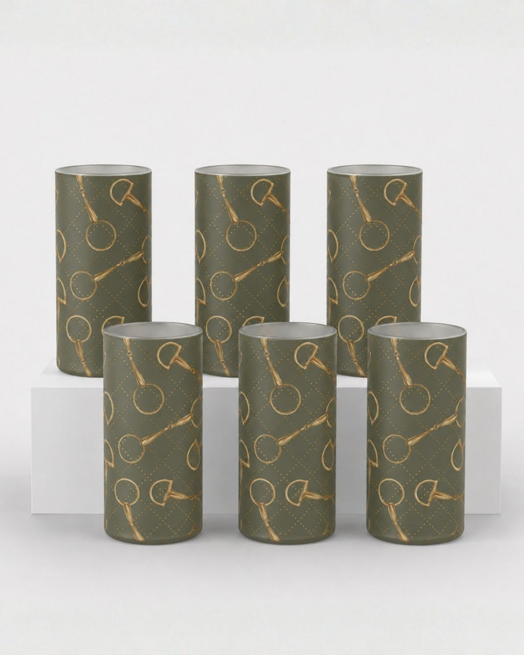 Six cylindrical decorative shot glasses in a muted olive green color, featuring a repeating metallic gold horse bit motif, arranged on a white display riser against a light gray background.