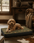 A golden doodle lies on a rectangular dog bed in a rustic living room. The bed has a green and tan horse-and-ribbed patterned top with dark charcoal sides.